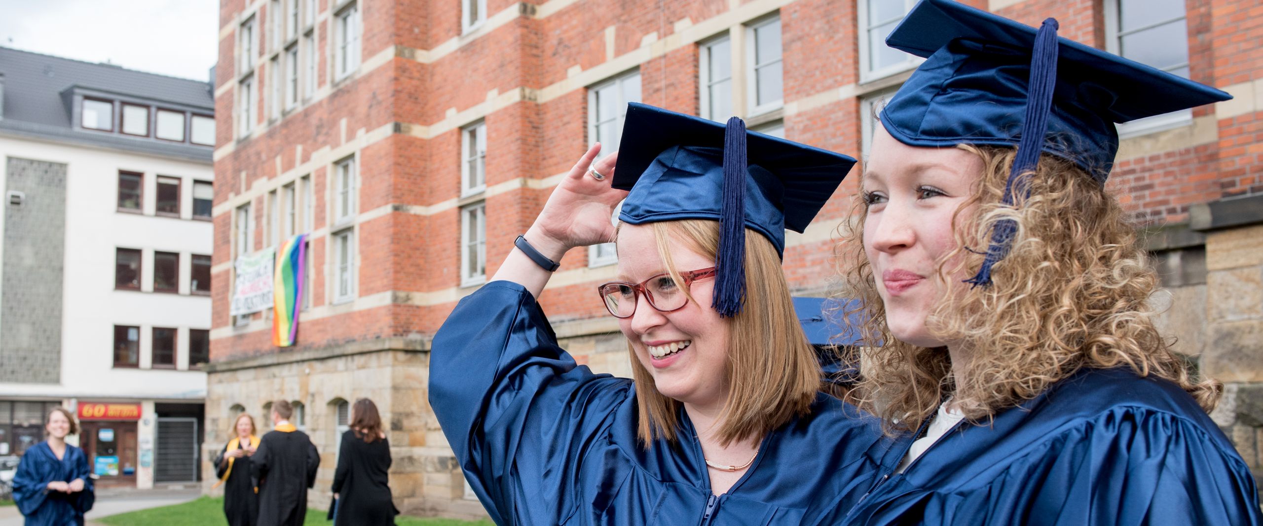 Abschlussfeier Studierende in Talar Zwei weibliche Studierende im Talar stehen vor dem M-Gebäude der HSB und posieren für ein Foto.