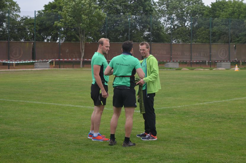 Eine Gruppe mit drei L&auml;ufern unterh&auml;lt sich auf einer Wiese.