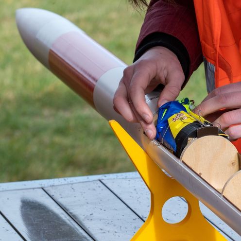 Kleine Rakete liegt auf einem Tisch. Zwei H&auml;nde sind zu sehen, die im Innenraum der Rakete etwas arbeiten. 