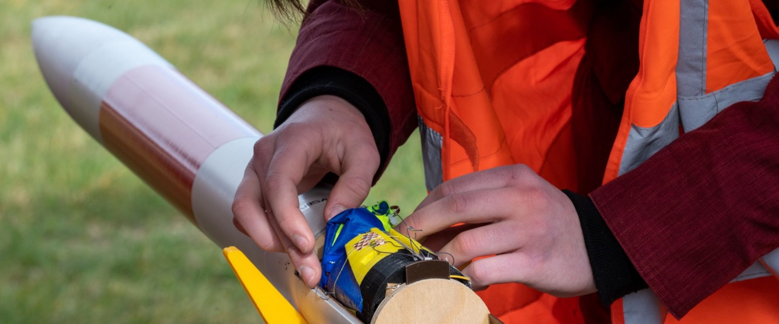 Kleine Rakete liegt auf einem Tisch. Zwei H&auml;nde sind zu sehen, die im Innenraum der Rakete etwas arbeiten. 