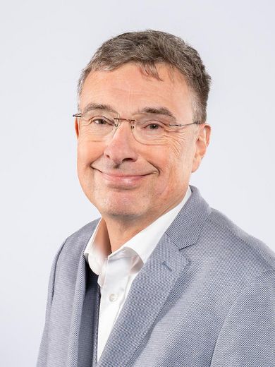Auf dem Foto ist Jens Eschenb&auml;cher zusehen. er hat kurze graue Haare. Er tr&auml;gt eine Brille und einen hellblauen Anzug mit wei&szlig;em Hemd. 