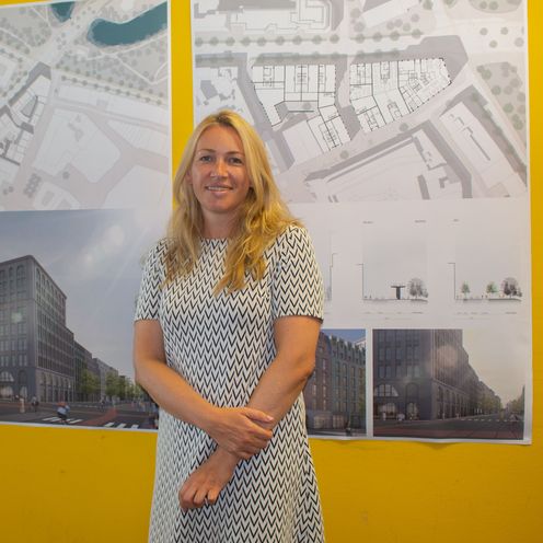 Masterabsolventin Marina Kaiser steht vor architektonischen Entw&uuml;rfen ihrer Masterarbeit, die an der Wand h&auml;ngen.