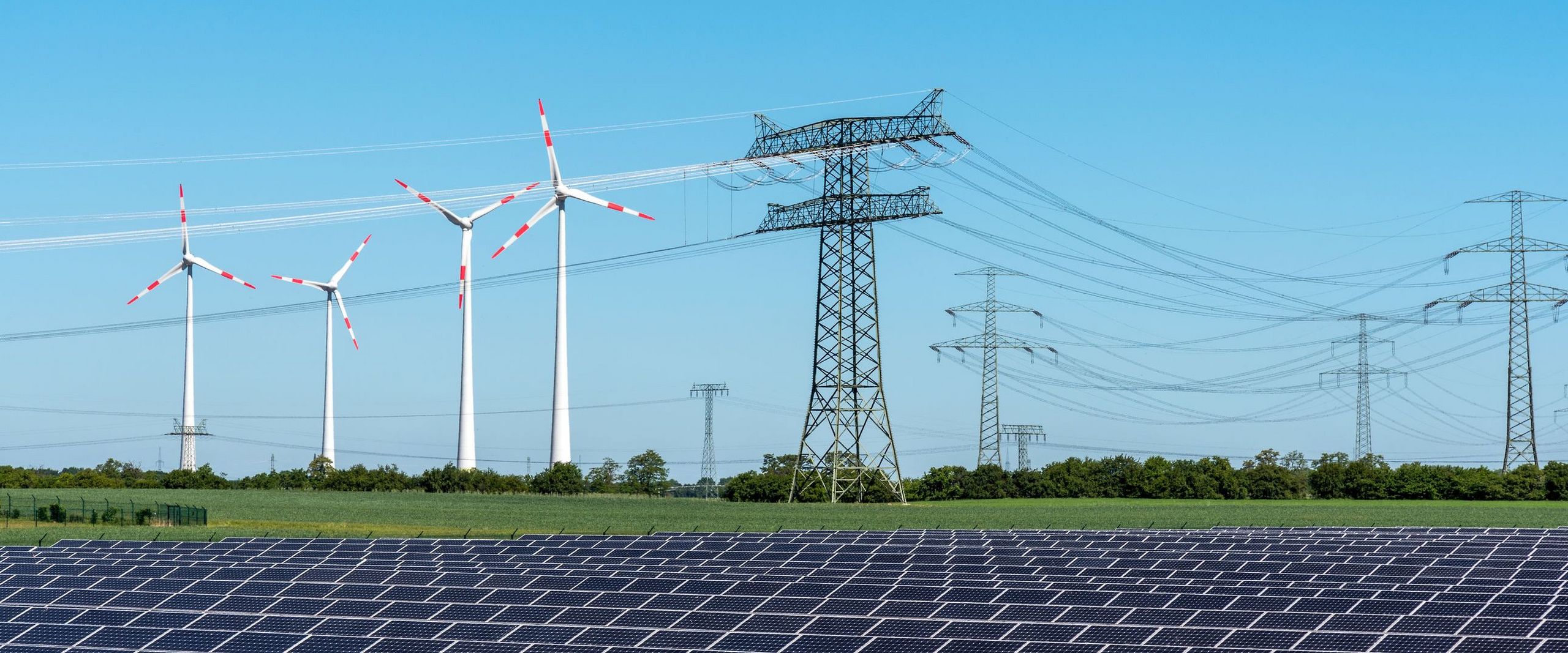 In einer Landschaft stehen Windräder, Solaranlagen und Strommasten nebeneinander