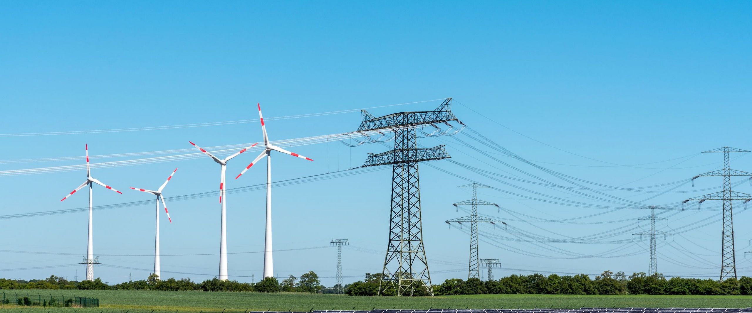 In einer Landschaft stehen Windräder, Solaranlagen und Strommasten nebeneinander