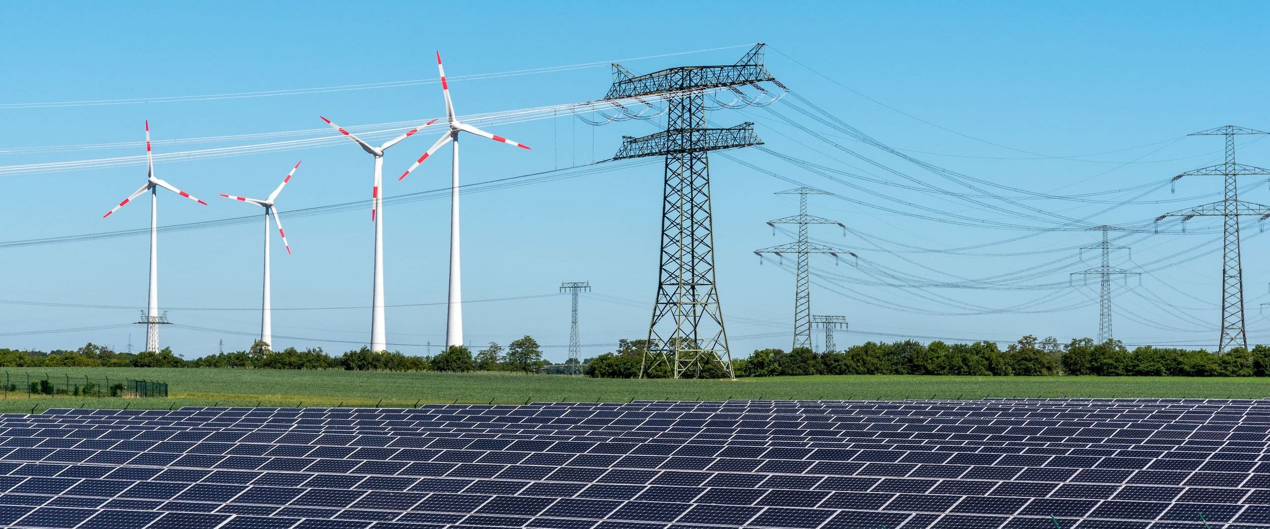 In einer Landschaft stehen Windräder, Solaranlagen und Strommasten nebeneinander