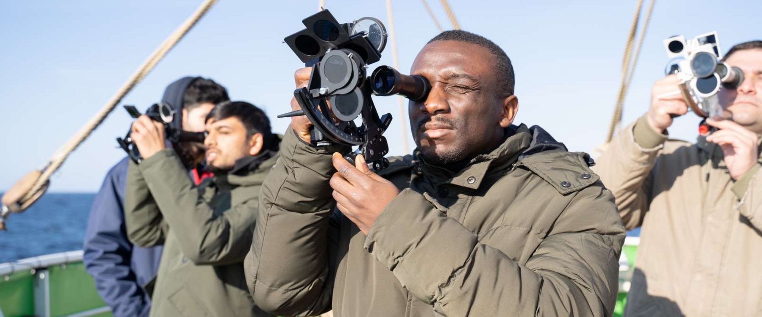 M&auml;nner auf einem Segelschiff schauen durch Sextanten.