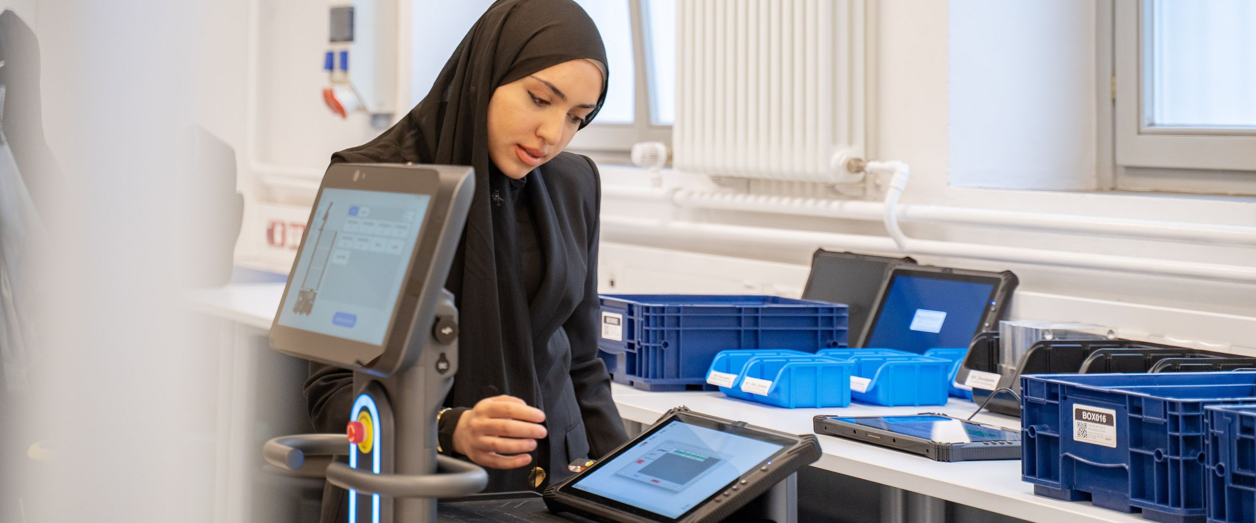 Junge Frau mit Kopftuch steht am Tisch udn arbeitet an einem Tablet