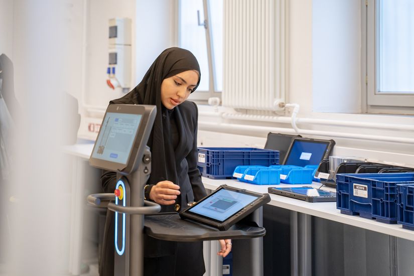 Junge Frau mit Kopftuch steht am Tisch udn arbeitet an einem Tablet