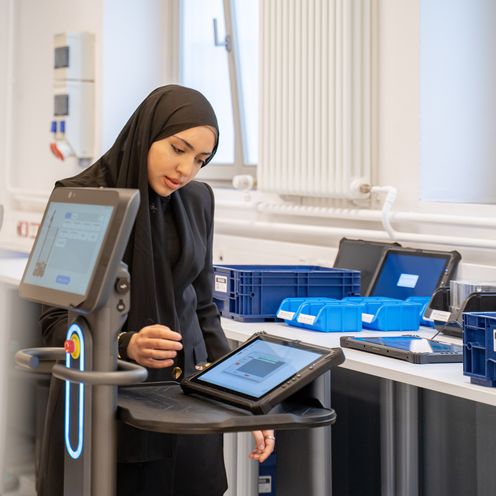 Junge Frau mit Kopftuch steht am Tisch udn arbeitet an einem Tablet