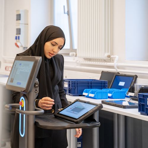Junge Frau mit Kopftuch steht am Tisch udn arbeitet an einem Tablet