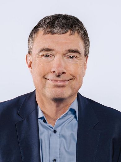 Auf dem Bild ist Jens Eschenbächer zusehen. Er hat kurze dunkle Haare und trägt ein hellblaues Hemd unter einem dunkelblauen Sakko. 