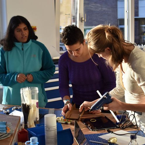 Drei junge Frauen arbeiten an einem Werktisch.