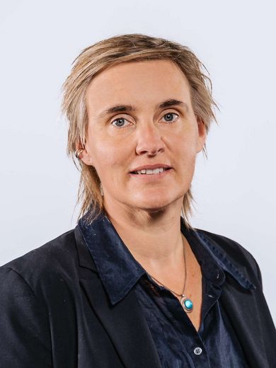 Auf dem Bild ist Katharina Rost zusehen. Sie trägt kurze blonde Haare und einen schwarzen Blazer über einer dunkelblauen Bluse.