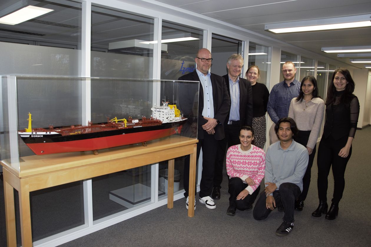 Gruppenbild mit Männern und Frauen. Links von ihnen steht ein Schiffsmodell in einer Vitrine.
