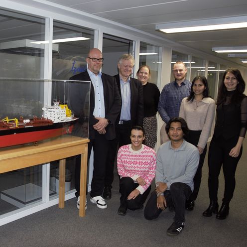 Gruppenbild mit M&auml;nnern und Frauen. Links von ihnen steht ein Schiffsmodell in einer Vitrine.