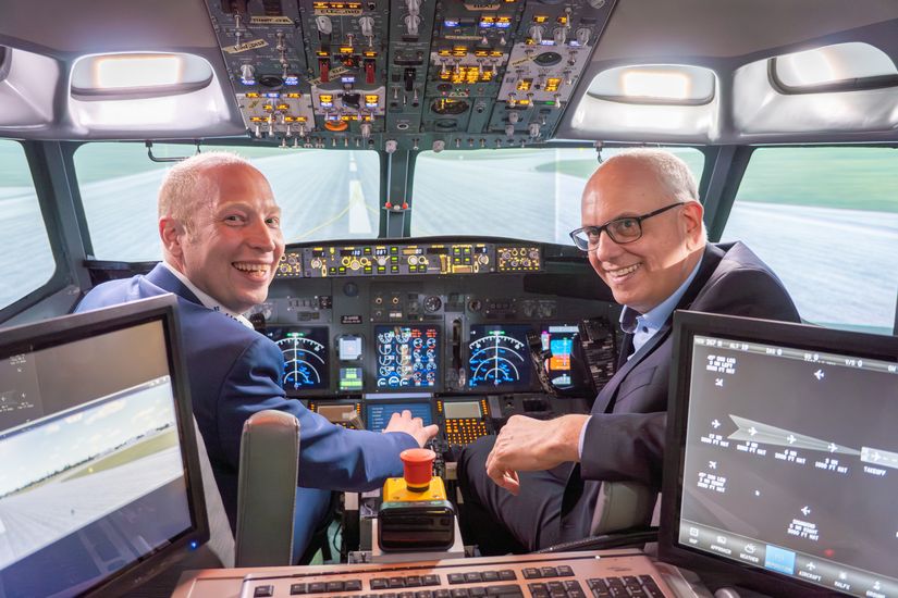 Zwei M&auml;nner sitzen in einem Flugzeugcockpit und schauen in die Kamera