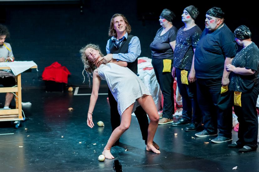 Bühnenszene aus dem Theaterstück "Peer Gynt" mit einer Gruppe Studierender. Im Vordergrund wird eine junge Frau von einem jungen Mann am Hals gepackt.