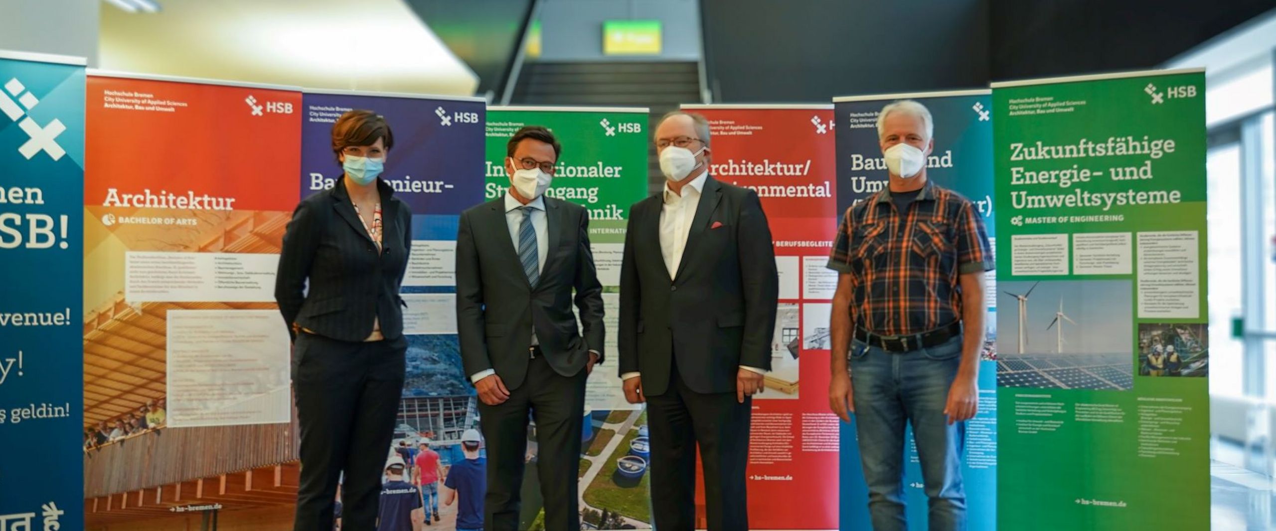 4 Personen mit Maske vor Rollups 