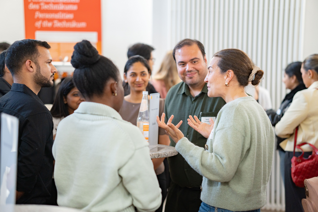 Career Service Menschen Menschen stehen um einen runden Stehtisch herum und unterhalten sich. Im Hintergrund sind weitere. Menschen zu sehen.