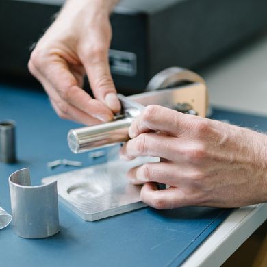 Eine Person schraubt an einem Stirlingmotor in Miniaturgröße.