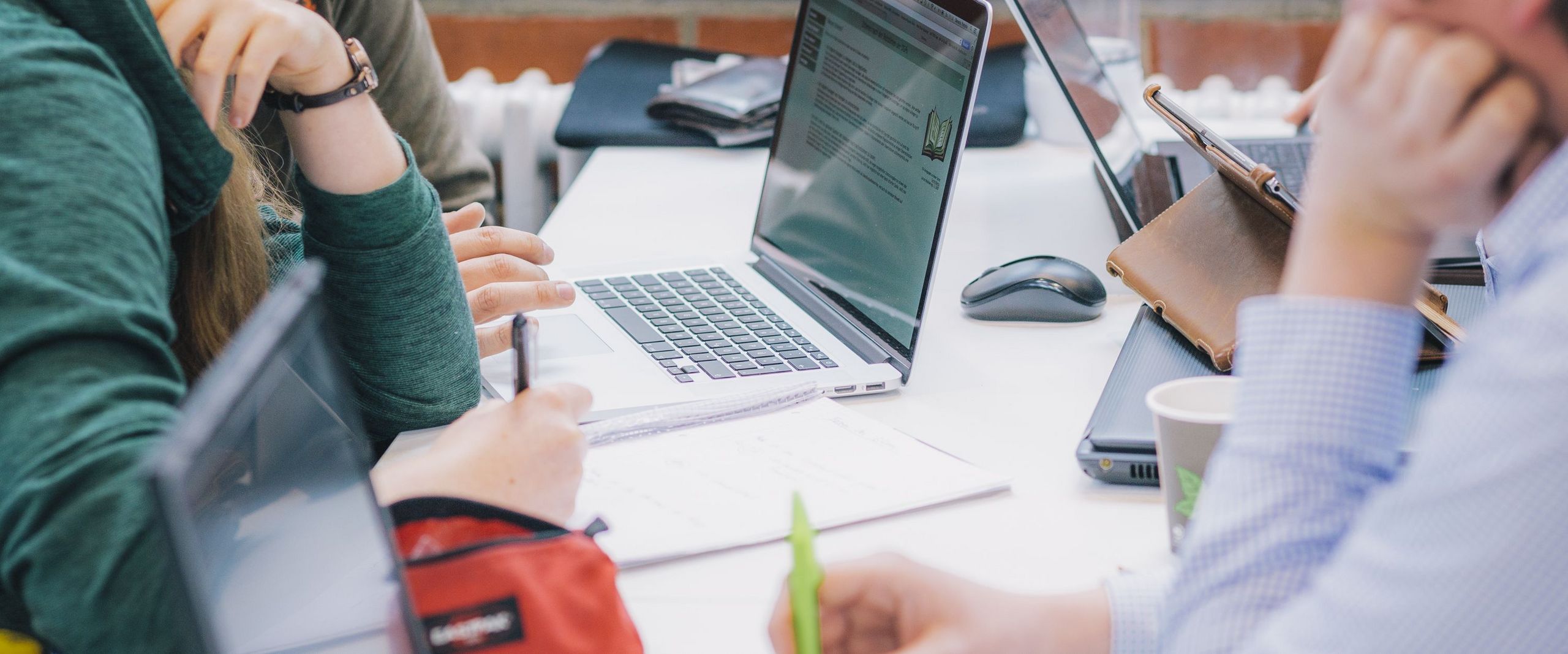mehrere Studierende sitzen mit Laptops zusammen und arbeiten an einer gemeinsamen Gruppenarbeit an einem Tisch in der Mensa.