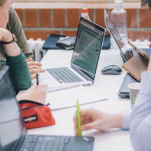 mehrere Studierende sitzen mit Laptops zusammen und arbeiten an einer gemeinsamen Gruppenarbeit an einem Tisch in der Mensa.