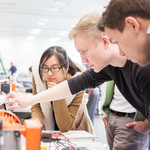 Junge M&auml;nner und eine Frau schauen gemeinsam auf eine Apparatur von Elektroger&auml;ten