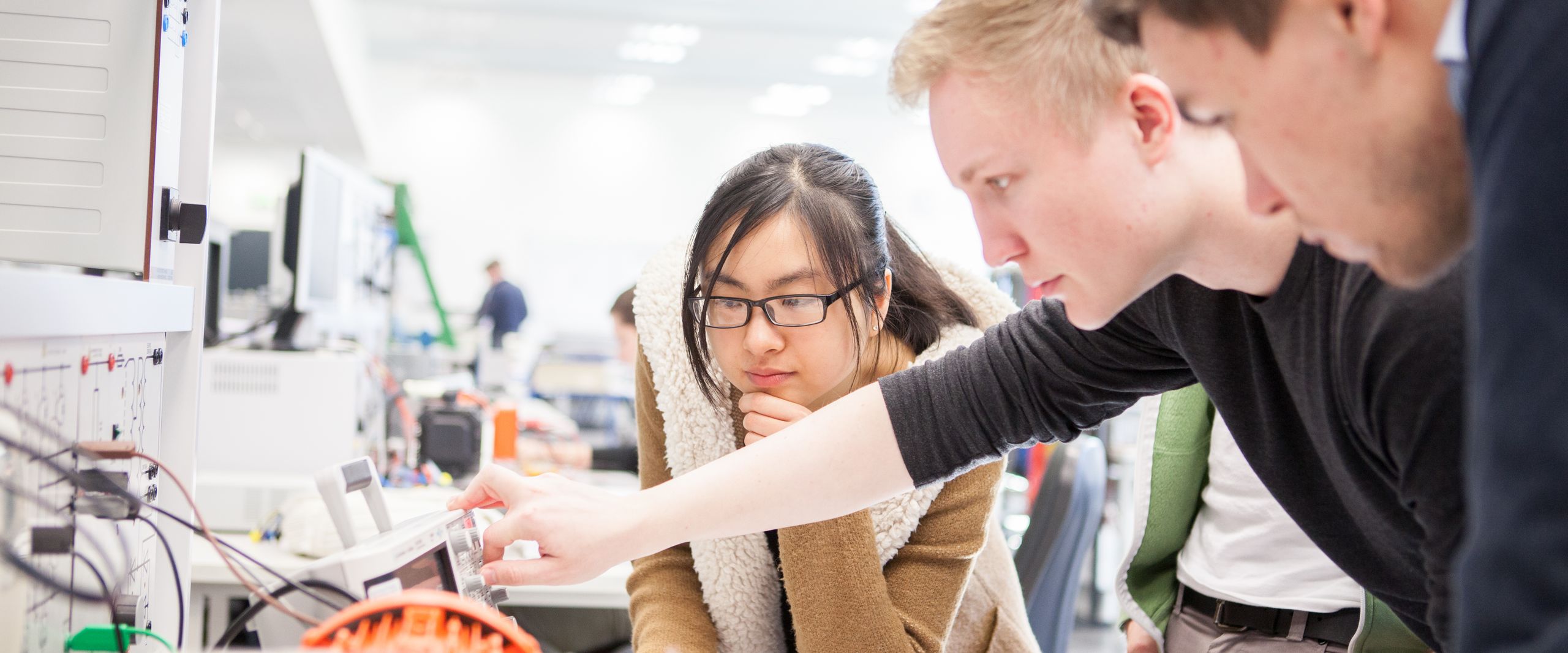 Junge M&auml;nner und eine Frau schauen gemeinsam auf eine Apparatur von Elektroger&auml;ten
