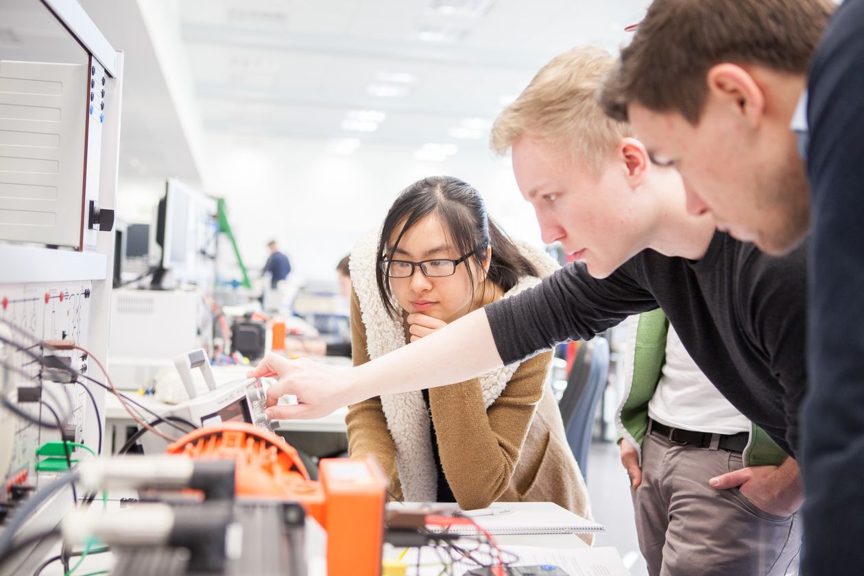Junge M&auml;nner und eine Frau schauen gemeinsam auf eine Apparatur von Elektroger&auml;ten