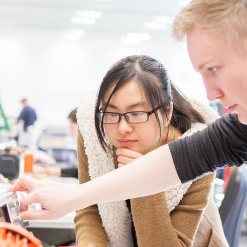 Junge M&auml;nner und eine Frau schauen gemeinsam auf eine Apparatur von Elektroger&auml;ten