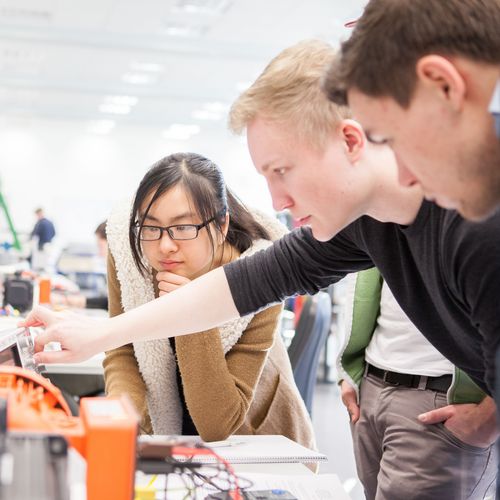 Junge M&auml;nner und eine Frau schauen gemeinsam auf eine Apparatur von Elektroger&auml;ten