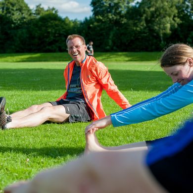 Trainer und Studierende beim Stretchen auf dem Sportplatz