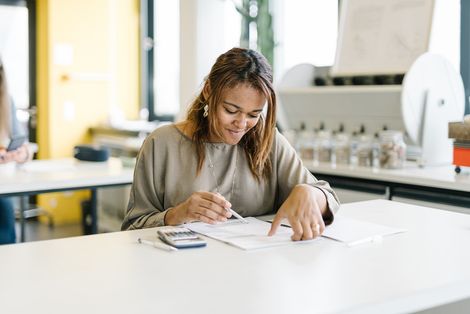 Eine Studentin sitzt an einem Tisch und ließt etwas.