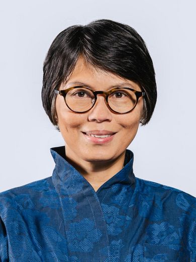 Auf dem Foto ist Suzette Suarez zusehen. Sie hat kurze schwarze Haare. Sie trägt eine Brille und eine blaue Jacke.