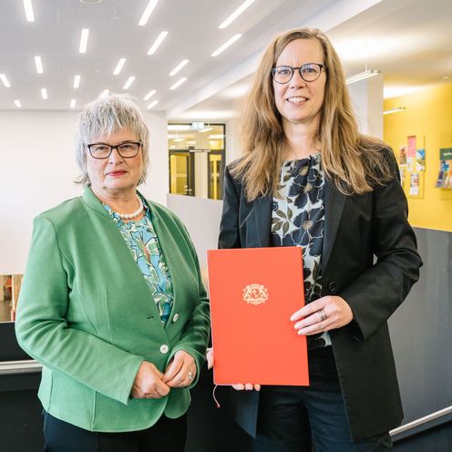 Bild mit zwei Frauen, die rechte h&auml;lt eine rote Urkunde.