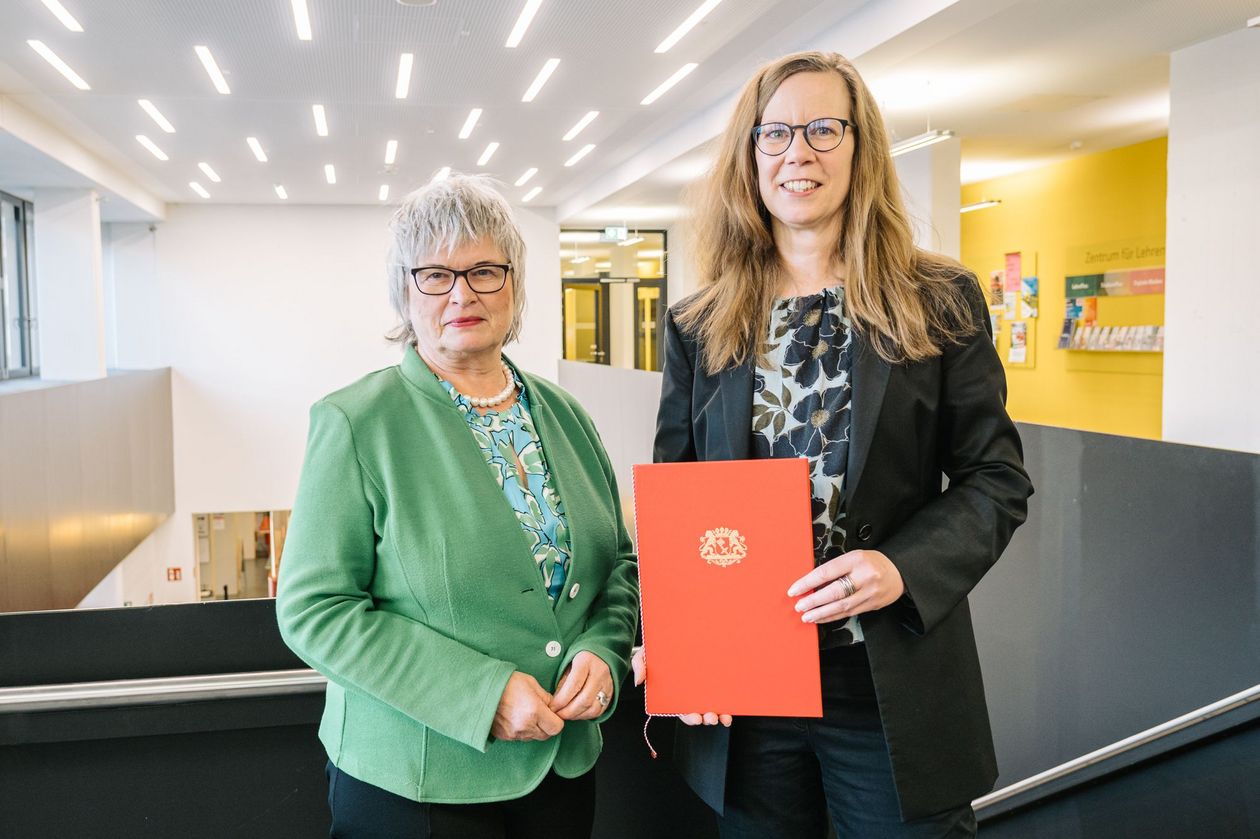 Bild mit zwei Frauen, die rechte hält eine rote Urkunde.