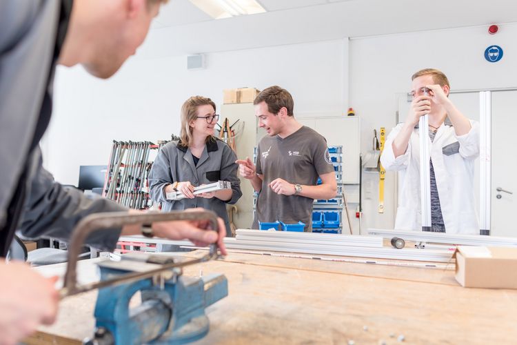 Eine Gruppe Studierende arbeitete an metallischen Bauteilen in einer Werkstatt.