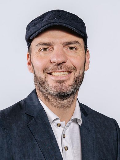 Auf dem Bild ist Elias Faethe zusehen. Er trägt eine Schiebermütze und ein weißes Hemd unter einem dunklen Sakko. 