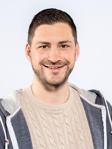 Auf dem Foto ist Jonas Unterholzner zusehen. Er hat kurze braune Haare und einen Drei-Tage-Bart. Er tr&auml;gt einen beigen Pullover unter einer blauen Sweatshirtjacke.