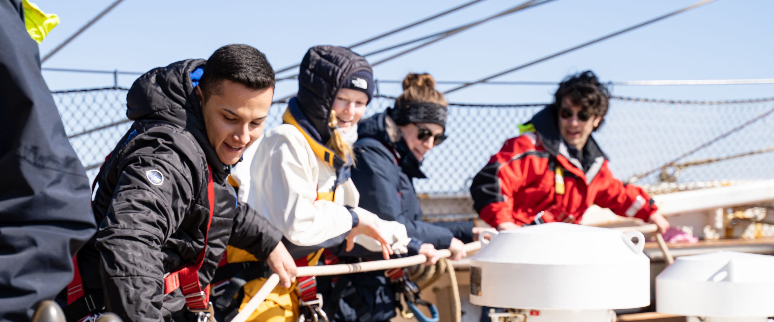 M&auml;nner und Frauen ziehen auf einem Segelschiff gemeisam an einem Tau.