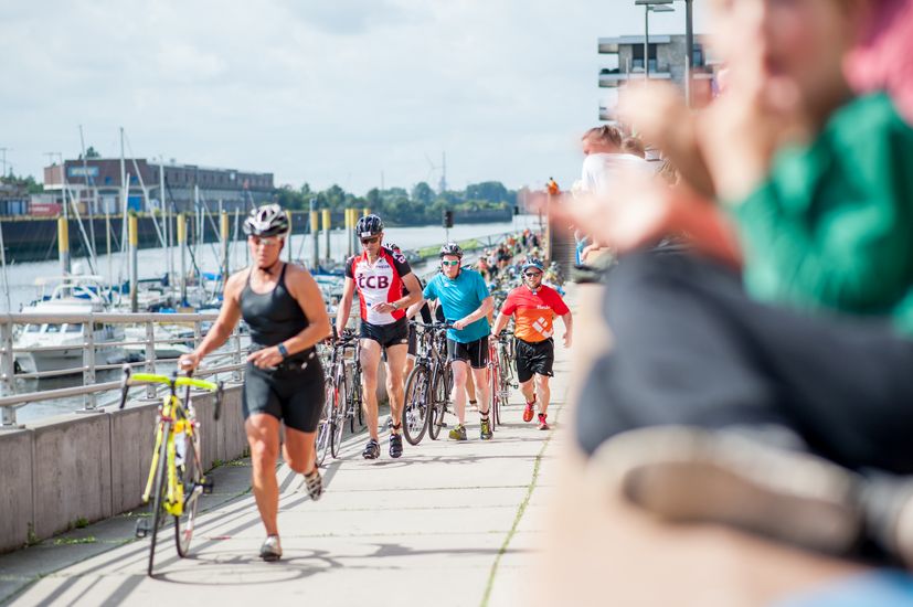 Männer laufen eine Steigung an der Weser hoch und schieben jeweils ein Fahrrad.