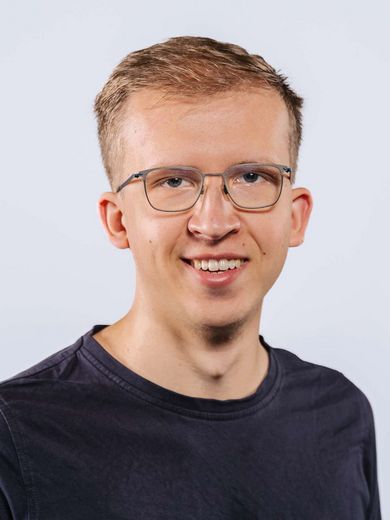 Auf dem Bild ist Tim Kruse zusehen. Er hat kurzes blondes Haar und trägt eine Brille und ein schwarzes T-Shirt.