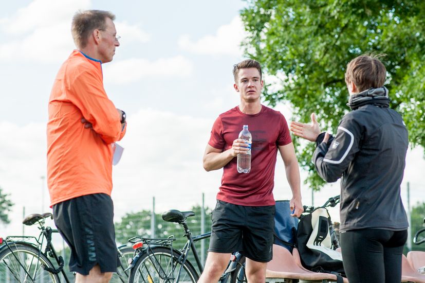 Drei Läufer stehen zusammen und unterhalten sich, sowie trinken etwas.