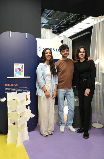 Three young people are standing next to a small white tower in an exhibition