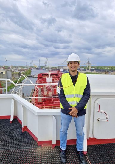 Man wearing a high-visibility waistcoat and hard hat stands on a tanker and looks into the camera.