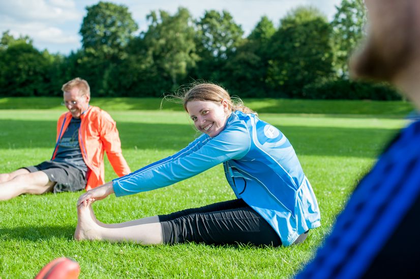 Projektteilnehmer sitzen auf einer Wiese und machen Dehn&uuml;bungen.