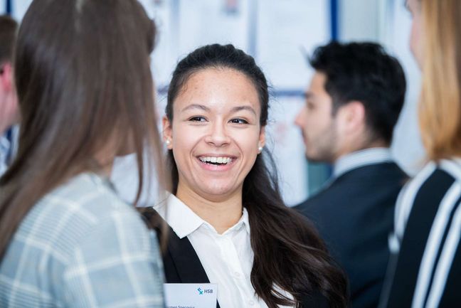 Junge Frau unterhält sich lächelnd mit einer anderen jungen Frau.