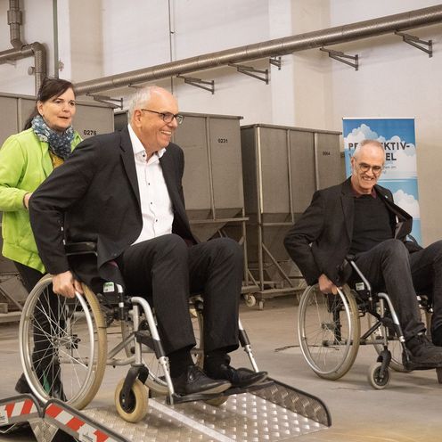 B&uuml;rgermeister Bovenschulte wird in einem Rollstuhl &uuml;ber ein Hindernis aus Metall geschoben. Daneben f&auml;hrt HSB-Prof. M&uuml;ller ebenfalls im Rollstuhl.