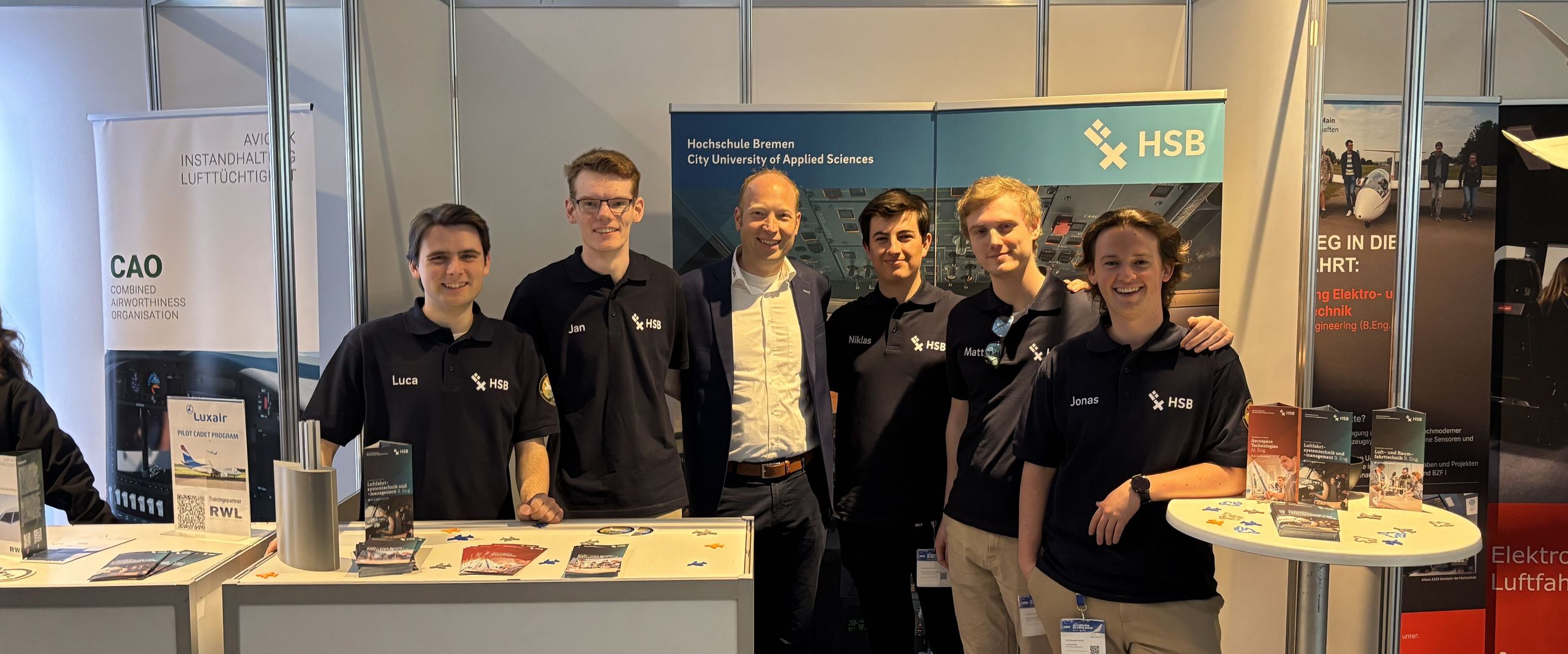 Studierende und Prod. Dr. von der Breie posieren vor dem HSB-Stand auf der Aero-Messe 2025. 