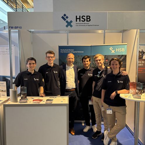 Studierende und Prod. Dr. von der Breie posieren vor dem HSB-Stand auf der Aero-Messe 2025. 